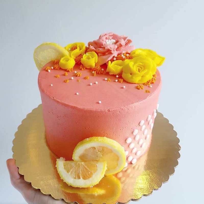 Coral vegan celebration cake topped with yellow sugar roses and fresh lemon