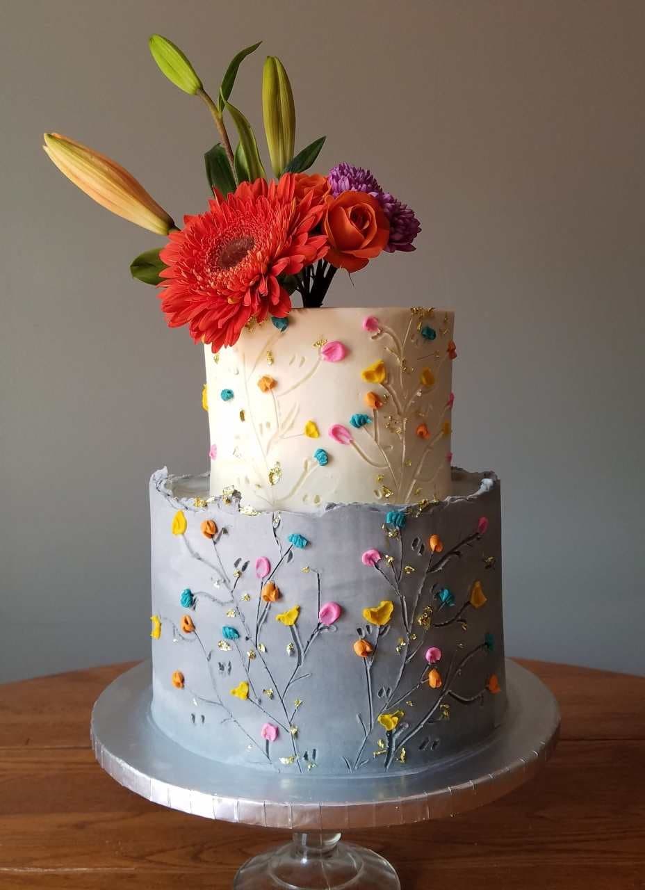 Two-tier vegan wedding cake in white and slate with hand-painted wildflowers, gold leaf, and a fresh-flower topper