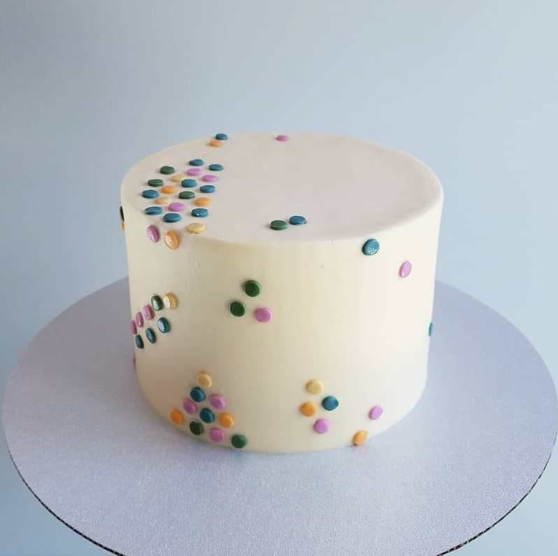 Minimalist vegan cake in ivory buttercream scattered with pastel confetti dots